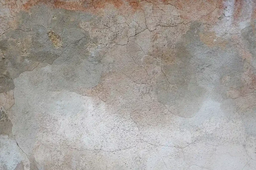 Close-up of an aged plaster wall with fine cracks, patches and an uneven historic surface